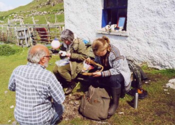 Archaeologists study the artefacts found in the various digs taking place on the Shiants 3 people studying objects outside a building