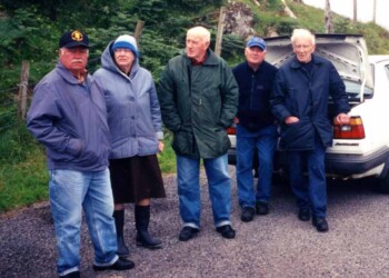 5 people standing on a road behind a car