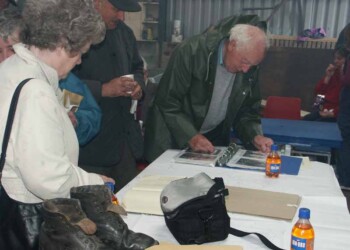 Alasdair Macdonald looking at our collection of old photos of Garyvard People looking at boots on a table