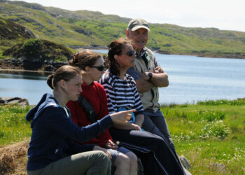 4 people sitting on a rock with loch in background