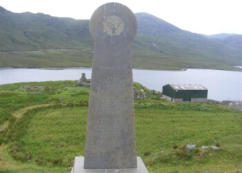 A monument with a loch, ruin and barn in the background